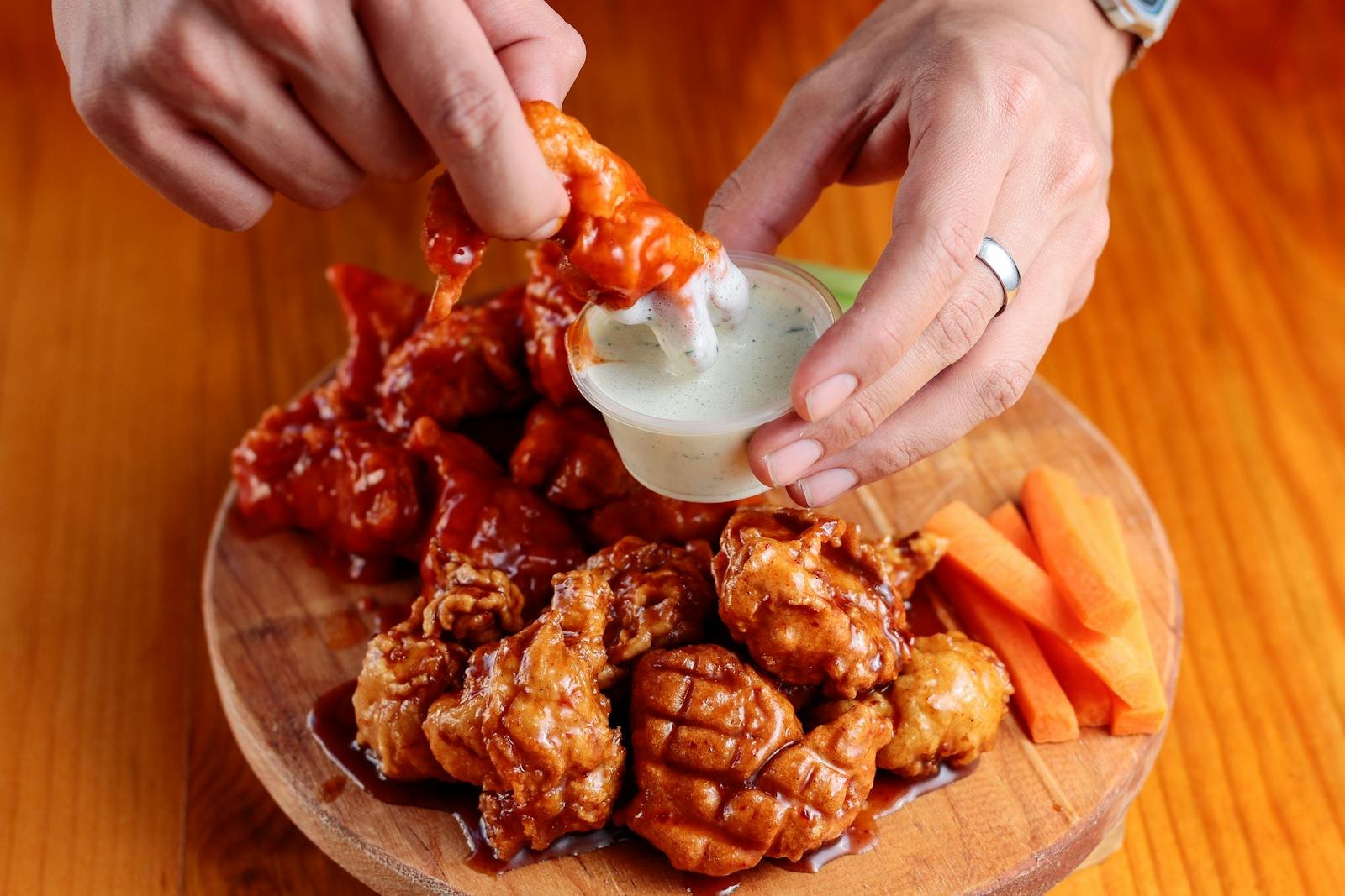 Délicieuses ailes de poulet sur un plateau en bois avec sauce et bâtonnets de carottes.